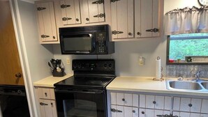 A kitchen with a microwave, stove, oven, and wooden cabinets. - A Cozy Camp Located 5 Minutes from State Gamelands and a Stocked Trout Stream… (Homer City)