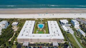 An aerial view of a hotel with a central pool, surrounded by parking and a beach in the background. - Grandma's Rest East (St. Augustine)