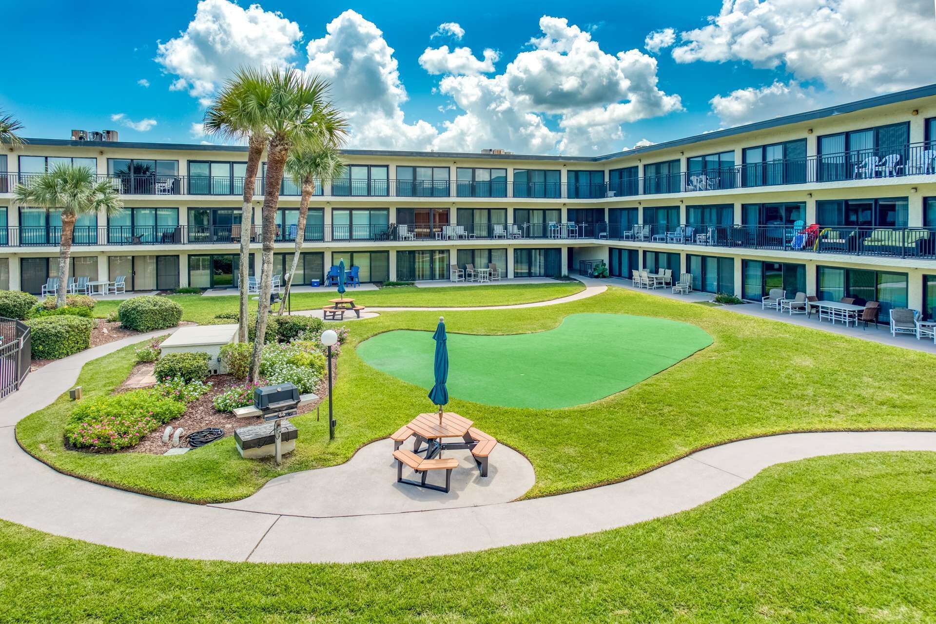 A hotel with multiple balconies, a well-maintained lawn, and outdoor seating areas.