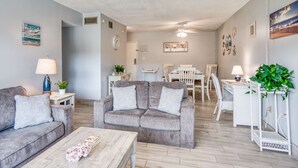 A living room with a grey sofa, a coffee table, and a dining area with white chairs and a table. - Grandma's Rest East (St. Augustine)