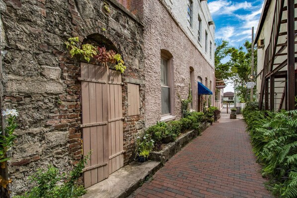 A narrow brick pathway flanked by buildings with stone walls and wooden shutters. - Grandma's Rest East (St. Augustine)