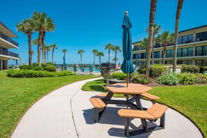 A poolside area with a picnic table and chairs, surrounded by palm trees and a clear blue sky. - Grandma's Rest East (St. Augustine)