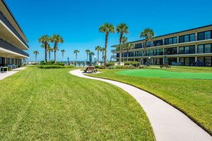 A well-maintained golf course with a clear pathway, surrounded by palm trees and modern buildings with balconies. - Grandma's Rest East (St. Augustine)