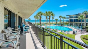 A balcony with wicker chairs and a pool area with lounge chairs and palm trees. - Grandma's Rest East (St. Augustine)