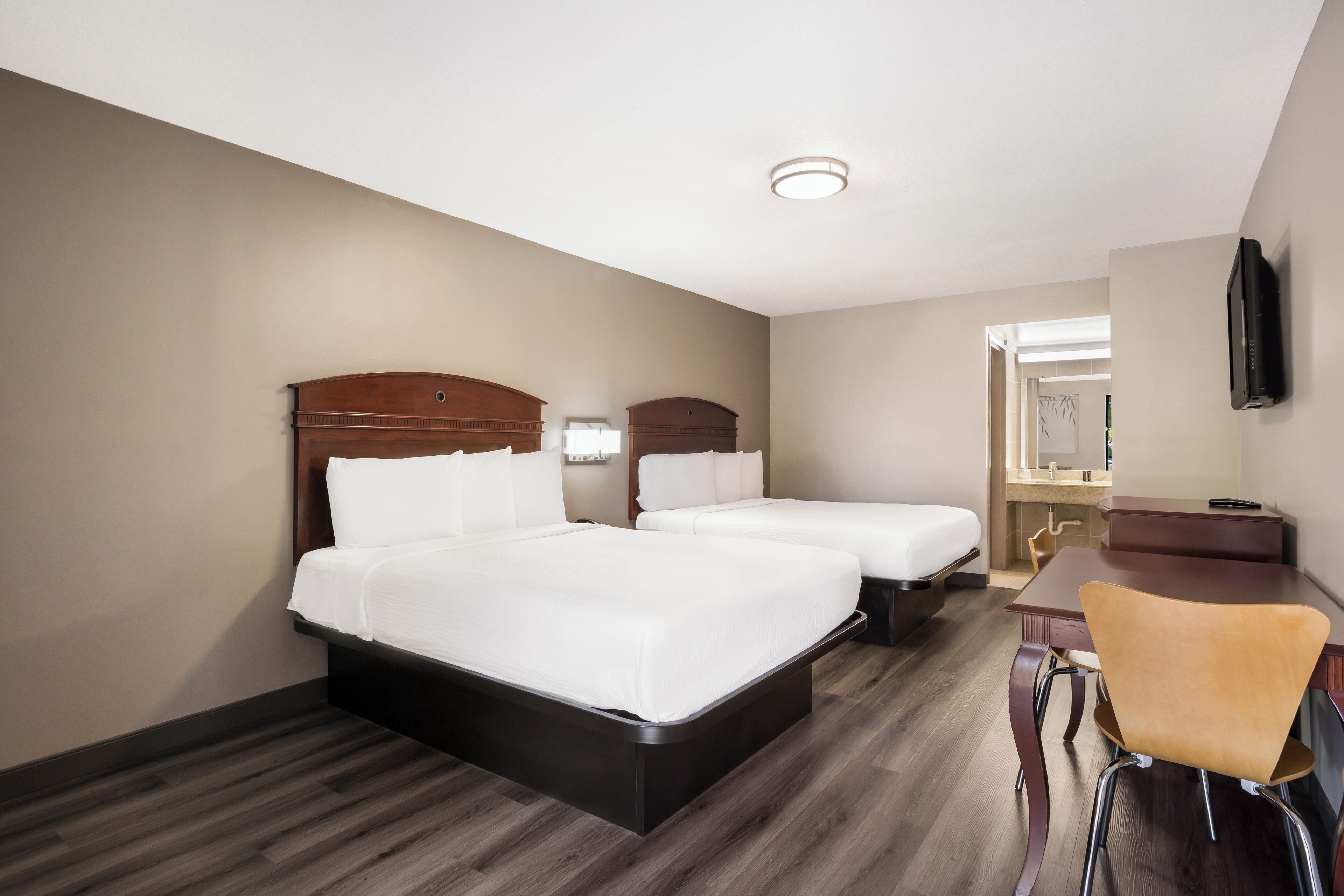 A hotel room with two beds, a desk, and a chair.