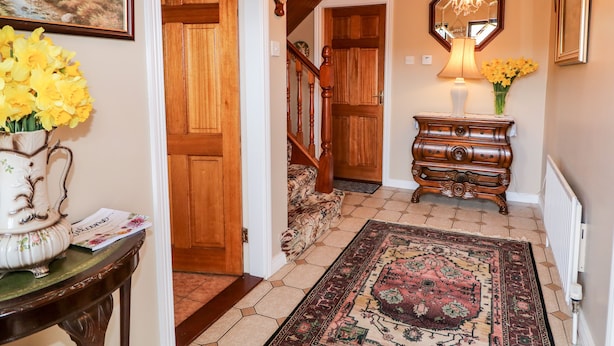Un pasillo con puerta de madera, escalera, espejo, lámpara y alfombra.