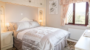 Un dormitorio con una cama grande, dos mesitas de noche con lámparas, un radiador, una ventana con cortinas y una pared decorada con una pintura floral.