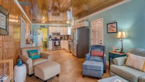 A cozy living room with a sofa, ottoman, and armchair, a kitchen with a refrigerator and stove, and a dining area with chairs. - Windswept Beach House (St. Augustine)
