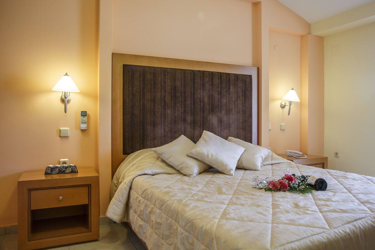Una cama bien hecha con cabecera, dos mesitas de noche con lámparas y un arreglo floral sobre la cama.