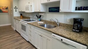 A kitchen with white cabinets, a stainless steel sink, a built-in oven, and a dishwasher. - Beach Cottage with a Private Hot Tub (Longboat Key)