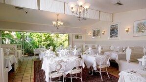 A dining area with white tables and chairs, chandeliers, and framed artwork on the walls. - Beach Cottage with a Private Hot Tub (Longboat Key)