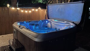 Un bain à remous avec une terrasse en bois et des guirlandes lumineuses en arrière-plan.