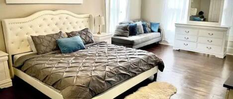 A bedroom with a large bed, a sofa, a dresser, and a mirror.