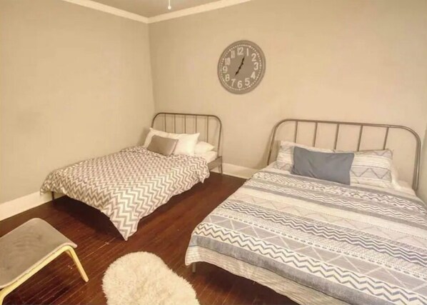 A bedroom with two single beds, a small chair, a fluffy rug, and a wall clock.