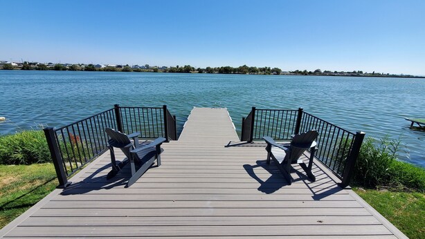 Een houten steiger met twee Adirondack stoelen gericht op een kalm meer.