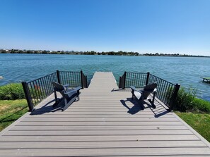 A wooden pier with two Adirondack chairs facing a calm lake. - Spacious Lakehouse Getaway. Private Dock with large fenced Backyard and Gameroom (Moses Lake)