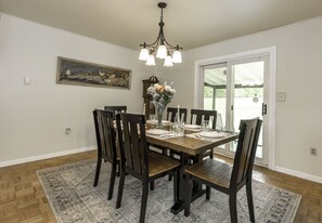A dining room with a wooden table set for six, surrounded by chairs, a chandelier, and a painting on the wall.