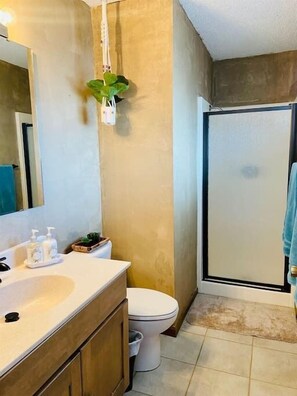 A bathroom with a white sink, wooden cabinets, a toilet, and a shower area.