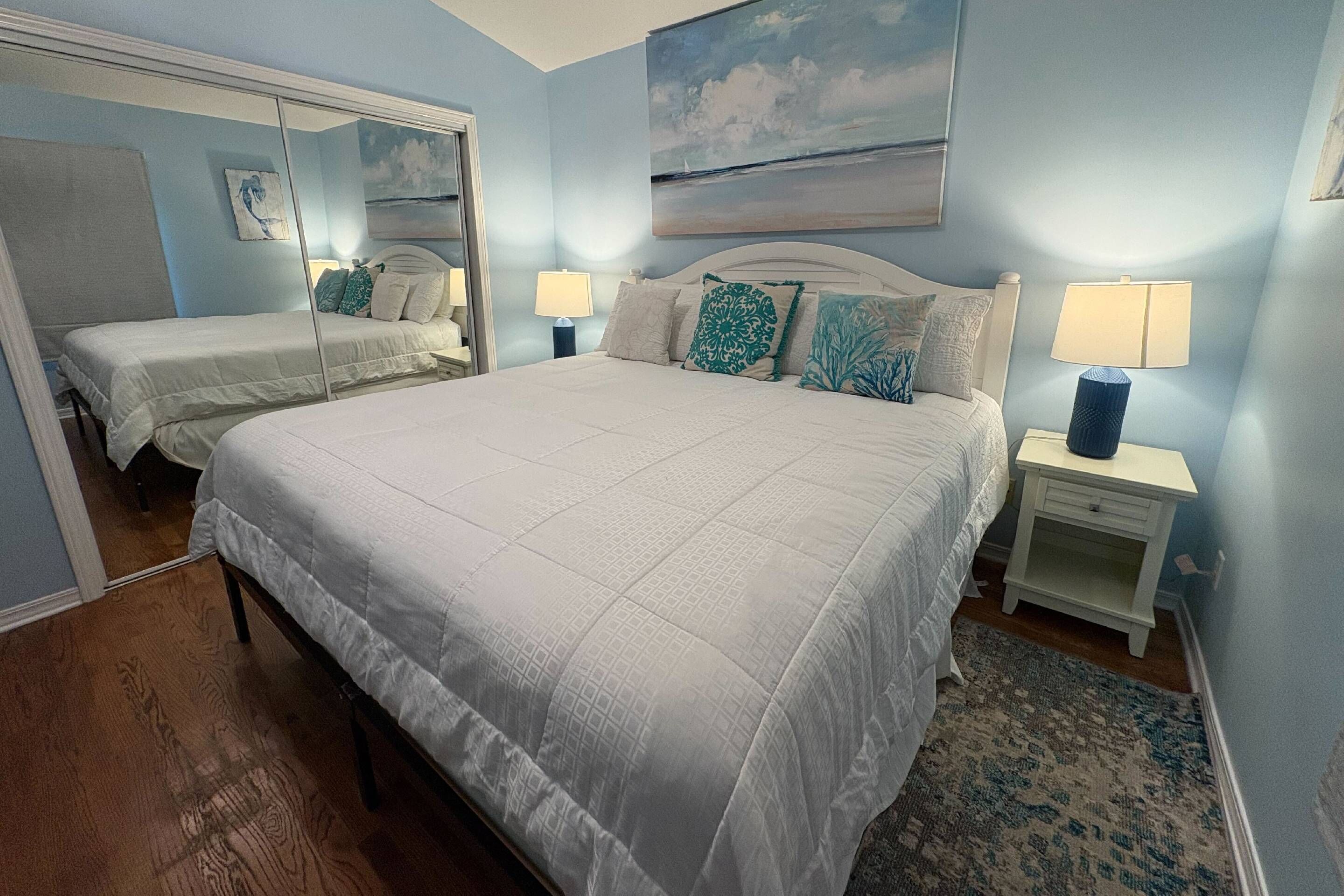 A bedroom with a large bed, two bedside tables with lamps, a mirror, and a painting on the wall.