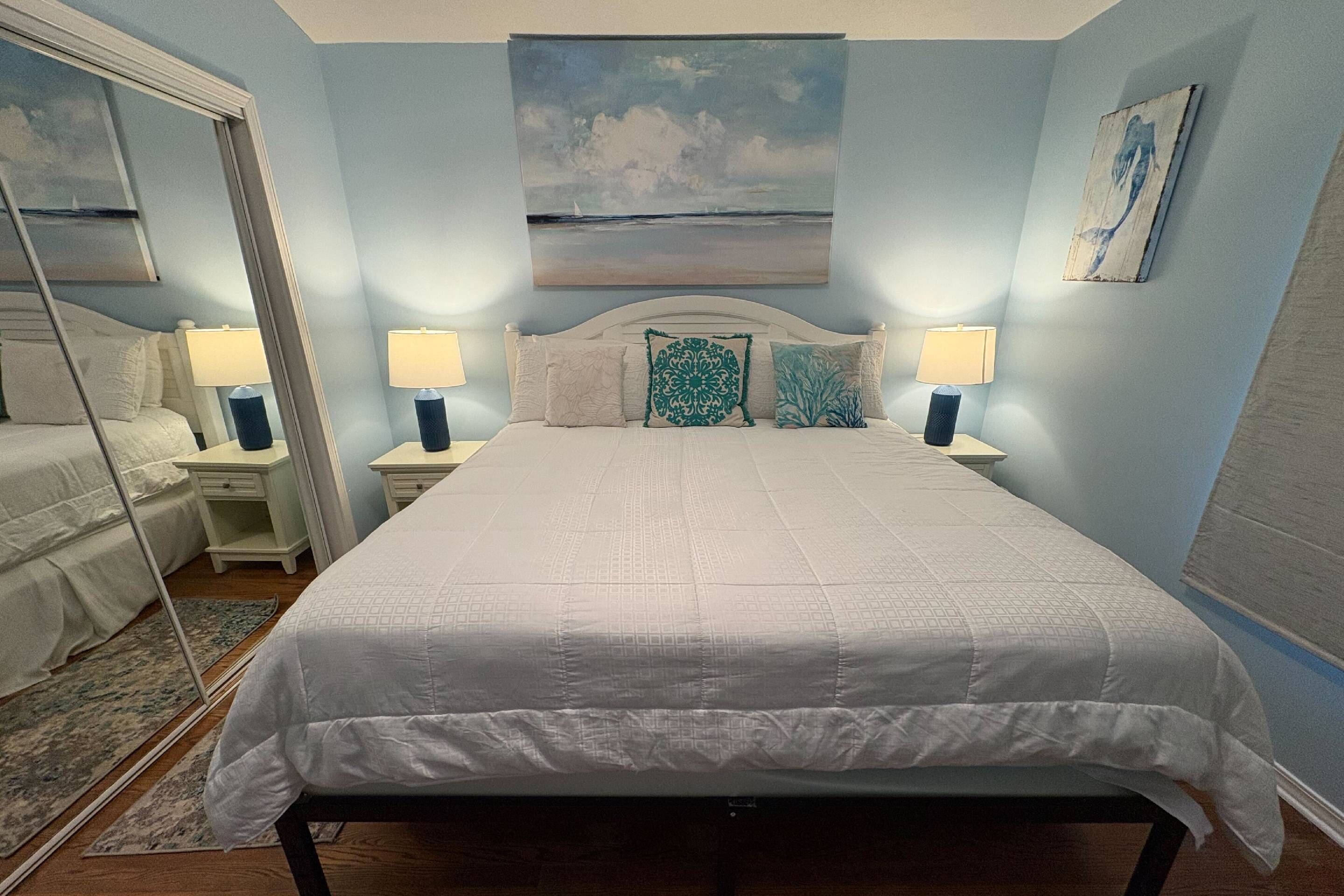 Une chambre à coucher avec un grand lit, deux tables de chevet avec des lampes, une tête de lit et un tableau au-dessus du lit.