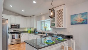 A modern kitchen with white cabinetry, stainless steel appliances, a granite countertop, and a large island with bar stools. - Chiquita Sun House (St. Augustine)