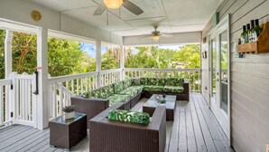 A covered porch with wicker furniture, ceiling fans, and a view of greenery. - Chiquita Sun House (St. Augustine)