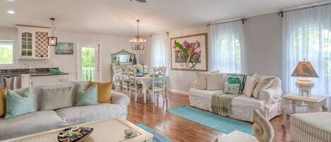 A spacious living room with a ceiling fan, a dining area with a table and chairs, and a kitchen in the background.
