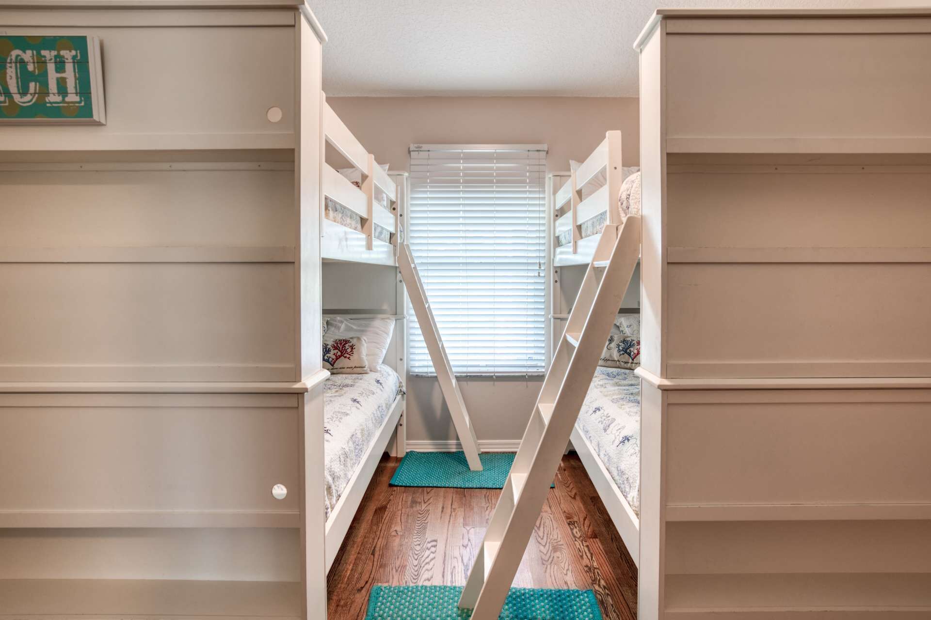 A bunk bed room with a ladder, wooden flooring, and a window with blinds.