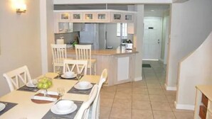 Zona pranzo con tavolo apparecchiato per quattro, cucina sullo sfondo e una scala che conduce a un altro livello.