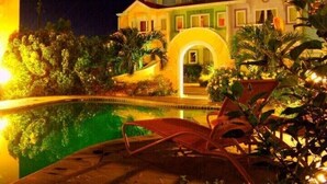 Un hotel con piscina, area relax con sedie e ingresso ben illuminato.