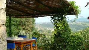 Patio esterno con tavolo di legno e sedie blu, immerso nel verde e con vista panoramica.
