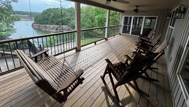 A covered porch with wooden flooring, a swing, and a view of a lake. - Large House with Front Row View of the Cliffs (Edgemont)