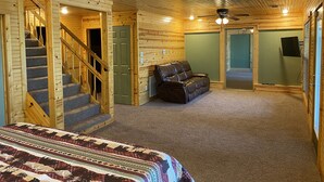 A log cabin interior with a staircase, a leather sofa, and a bed with a patterned blanket. - Large House with Front Row View of the Cliffs (Edgemont)