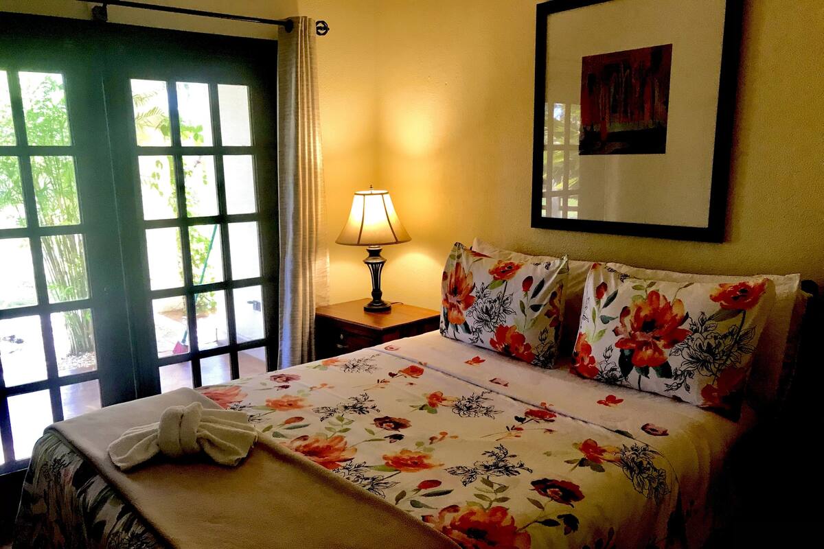 A bedroom with a bed, a bedside lamp, a window with curtains, and a framed picture on the wall.