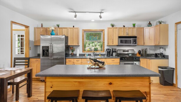 Une cuisine moderne avec des meubles en bois, un réfrigérateur en acier inoxydable, un four à micro-ondes et un grand îlot central doté de tabourets.