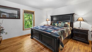Une chambre avec un grand lit, un plancher en bois, une fenêtre donnant sur un beau paysage et deux tables de chevet avec des lampes.