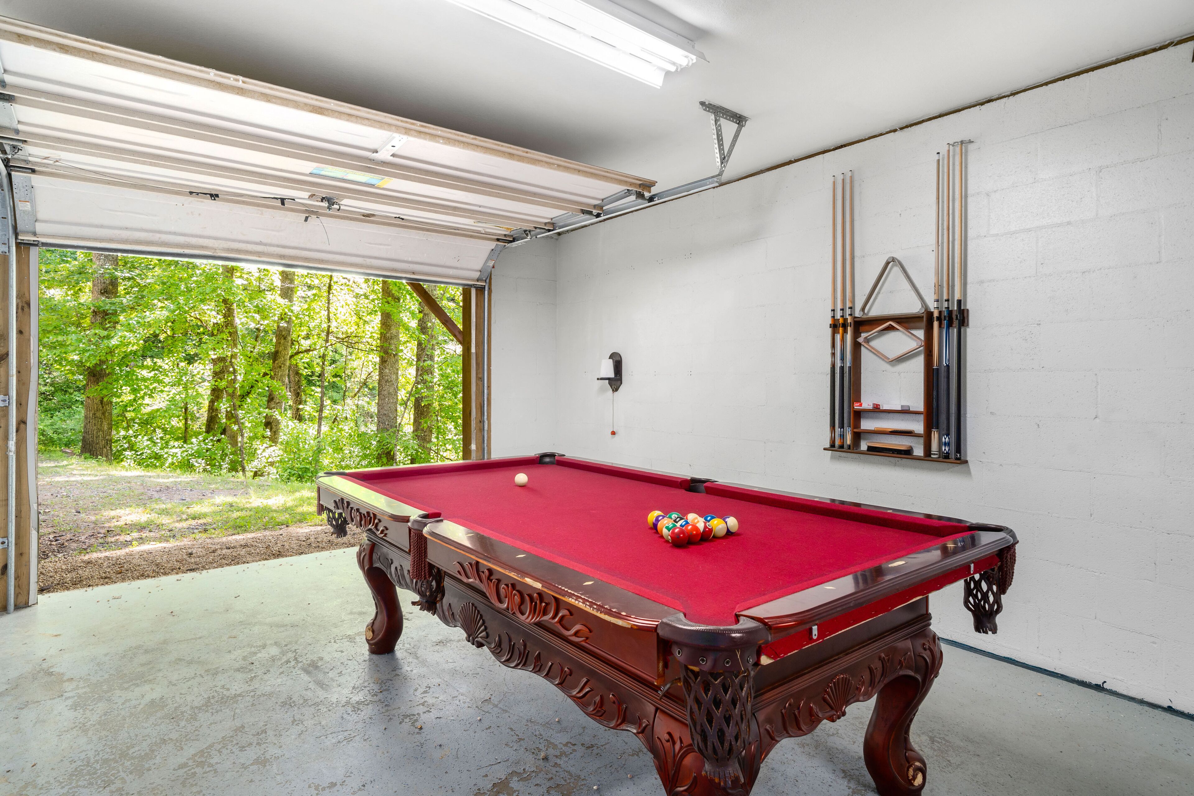 A pool table in a garage with a view of trees.