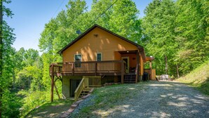 Une cabane en bois avec un porche, une allée en gravier et un paysage boisé en arrière-plan.