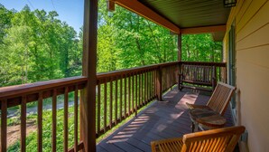 Une véranda en bois avec une balustrade, deux chaises en bois et une table.