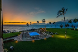 A pool area with a view of the ocean, surrounded by palm trees and a sunset.