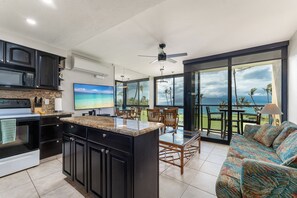 A modern kitchen with a large island, a dining area with a view, and a living space with a sofa. - 308 – Deluxe Oceanfront One Bedroom Unit with A/C! (Kihei)
