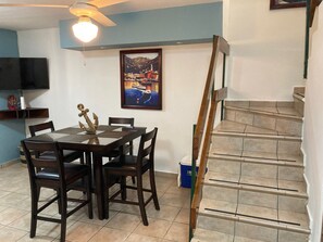 Ein Essbereich mit Tisch und Stühlen, einem Bild an der Wand, einem Deckenventilator und einer Treppe.