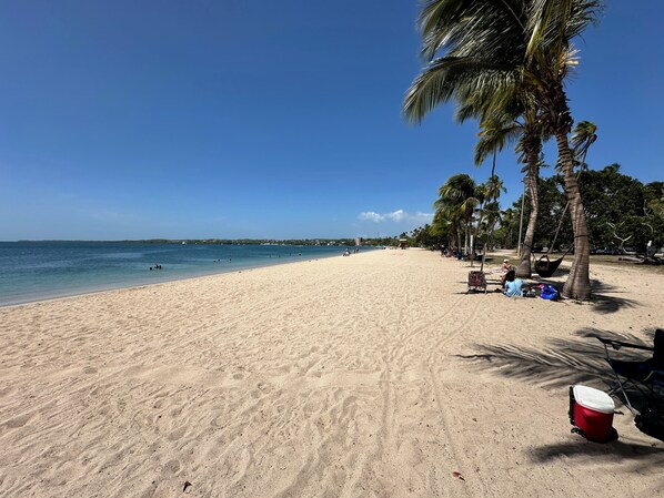 A beach with a clear sky, palm trees, and a red cooler on the sand. - NEW! Walking distance to Boqueron ‘Poblado’, townhouse w/amazing views, sleeps 8 (Boqueron)
