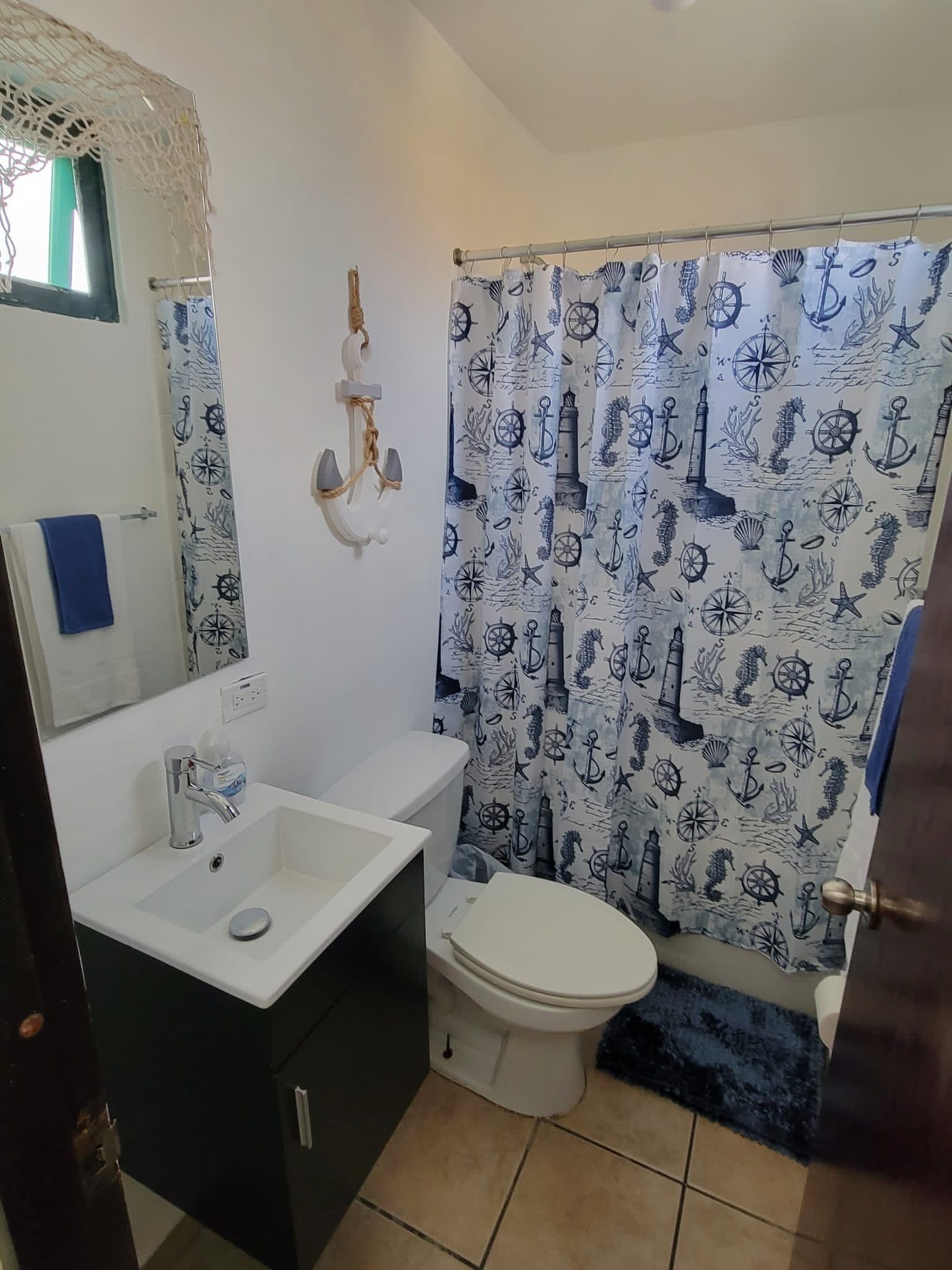 A bathroom with a nautical-themed shower curtain, a white sink, and a toilet.