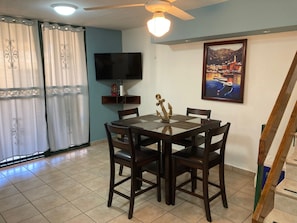 A dining area with a table and chairs, a television on the wall, and a painting.