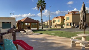 A playground with a red slide and a blue climbing structure, surrounded by buildings with a modern architectural style. - NEW! Walking distance to Boqueron ‘Poblado’, townhouse w/amazing views, sleeps 8 (Boqueron)