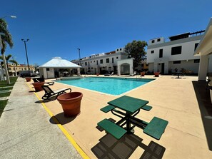 A pool area with lounge chairs and tables, surrounded by buildings.