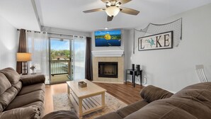 Ein Wohnzimmer mit Kamin, einem darüber befestigten Fernseher und Seeblick durch die Glasdoor.