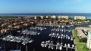 Un puerto deportivo con numerosas embarcaciones amarradas, rodeado de edificios residenciales y una vista despejada del océano.