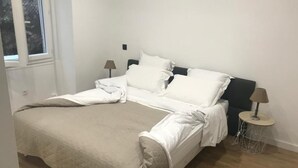 A bedroom with a bed, two bedside tables, and a window. - Apartment (nice)